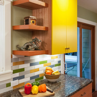 Idées déco pour une petite arrière-cuisine parallèle éclectique avec un évier encastré, un placard à porte plane, des portes de placard jaunes, un plan de travail en granite, une crédence multicolore, une crédence en carreau de céramique, un électroménager en acier inoxydable, un sol en bois brun et aucun îlot.