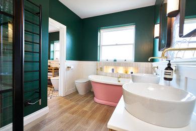 Cette image montre une grande salle de bain bohème en bois brun pour enfant avec un placard à porte shaker, meuble-lavabo sur pied, une baignoire indépendante, une douche d'angle, WC à poser, un carrelage rose, des carreaux de céramique, un mur vert, un sol en carrelage de porcelaine, un plan vasque, un sol marron, une cabine de douche à porte battante, du lambris, un plan de toilette en quartz, un plan de toilette blanc et meuble double vasque.