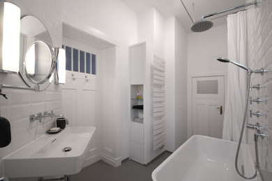 Kleines Modernes Badezimmer mit flächenbündigen Schrankfronten, weißen Schränken, freistehender Badewanne, Duschbadewanne, Wandtoilette, weißen Fliesen, Keramikfliesen, weißer Wandfarbe, Wandwaschbecken, grauem Boden und Duschvorhang-Duschabtrennung in Berlin