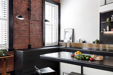 Photo of an industrial l-shaped kitchen in Melbourne with an undermount sink, flat-panel cabinets, black cabinets, black splashback, mosaic tile splashback, dark hardwood floors, with island, brown floor and black benchtop.