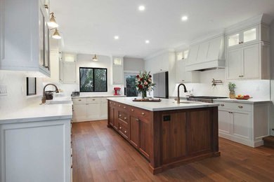 This is an example of a large contemporary l-shaped kitchen/diner in San Francisco with a belfast sink, shaker cabinets, white cabinets, composite countertops, white splashback, metro tiled splashback, stainless steel appliances, medium hardwood flooring, an island, brown floors and white worktops.
