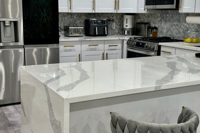Example of a mid-sized trendy u-shaped vinyl floor, gray floor and coffered ceiling eat-in kitchen design in New York with an undermount sink, shaker cabinets, white cabinets, quartzite countertops, gray backsplash, marble backsplash, stainless steel appliances, an island and multicolored countertops