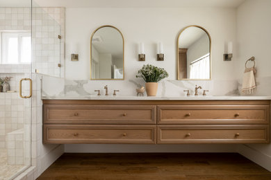 Inspiration for a mid-sized contemporary master white tile and ceramic tile laminate floor, brown floor and double-sink corner shower remodel in Orange County with raised-panel cabinets, medium tone wood cabinets, white walls, an undermount sink, quartz countertops, a hinged shower door, white countertops, a niche and a floating vanity