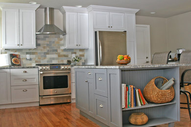 Eat-in kitchen - large contemporary l-shaped medium tone wood floor eat-in kitchen idea in Seattle with a farmhouse sink, recessed-panel cabinets, white cabinets, granite countertops, beige backsplash, subway tile backsplash, stainless steel appliances and an island