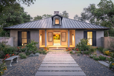 Imagen de fachada de casa beige y marrón tradicional renovada grande de una planta con revestimiento de estuco, tejado a cuatro aguas y tejado de metal