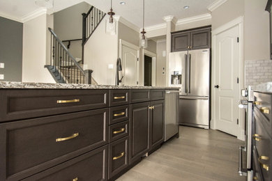 Example of a mid-sized transitional l-shaped medium tone wood floor and brown floor open concept kitchen design in Calgary with an undermount sink, raised-panel cabinets, dark wood cabinets, granite countertops, gray backsplash, porcelain backsplash, stainless steel appliances and an island