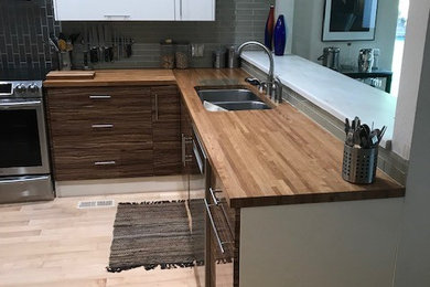 Example of a small trendy l-shaped bamboo floor eat-in kitchen design in Other with a double-bowl sink, flat-panel cabinets, stainless steel appliances, wood countertops, gray backsplash, glass tile backsplash and no island