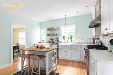 Large farmhouse l-shaped light wood floor and brown floor enclosed kitchen photo in Seattle with a farmhouse sink, shaker cabinets, white cabinets, quartz countertops, white backsplash, subway tile backsplash, stainless steel appliances, an island and yellow countertops