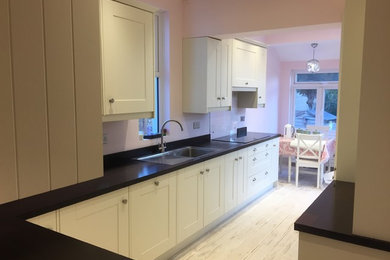Design ideas for a large traditional galley kitchen/diner in Other with a single-bowl sink, shaker cabinets, beige cabinets, wood worktops, glass sheet splashback, black appliances, ceramic flooring and white floors.