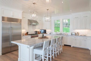 Inspiration for a beach style l-shaped kitchen in Toronto with an undermount sink, recessed-panel cabinets, white cabinets, white splashback, subway tile splashback, stainless steel appliances, light hardwood floors, with island, beige floor and grey benchtop.