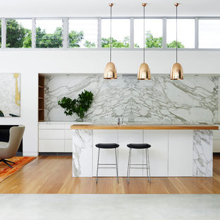 Modelo de cocina actual, extra grande, abierta, con armarios con paneles lisos, puertas de armario blancas, encimera de mármol, una isla, salpicadero blanco y electrodomésticos con paneles