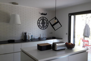 Mid-sized contemporary l-shaped eat-in kitchen in Angers with an undermount sink, flat-panel cabinets, white cabinets, quartzite benchtops, white splashback, brick splashback, stainless steel appliances, light hardwood floors, with island and black benchtop.
