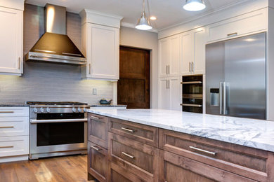 Inspiration for a transitional medium tone wood floor and brown floor kitchen remodel in Other with an undermount sink, white cabinets, quartz countertops, beige backsplash, porcelain backsplash, stainless steel appliances, an island, gray countertops and shaker cabinets