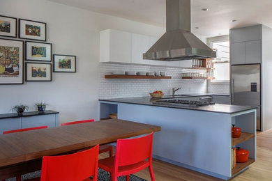Photo of a mid-sized contemporary u-shaped eat-in kitchen in San Francisco with an undermount sink, flat-panel cabinets, white cabinets, white splashback, subway tile splashback, stainless steel appliances, light hardwood floors and a peninsula.