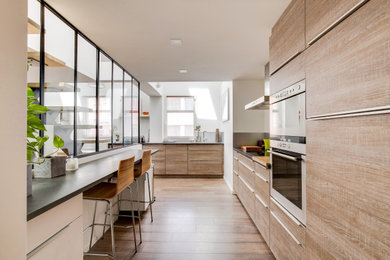 Contemporary l-shaped kitchen in Paris with flat-panel cabinets, light wood cabinets, stainless steel appliances, medium hardwood floors, a peninsula, brown floor and grey benchtop.