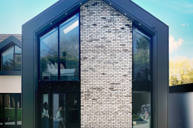 Diseño de fachada de casa gris y gris actual de tamaño medio de dos plantas con revestimiento de metal, tejado a dos aguas, tejado de varios materiales y panel y listón