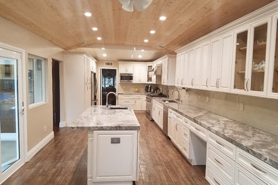 Inspiration for a large transitional l-shaped dark wood floor and brown floor enclosed kitchen remodel in Los Angeles with an undermount sink, raised-panel cabinets, white cabinets, granite countertops, beige backsplash, glass tile backsplash, stainless steel appliances and an island