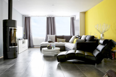 Exemple d'un salon tendance de taille moyenne et ouvert avec un mur jaune, un sol en carrelage de porcelaine, un poêle à bois, un manteau de cheminée en métal, un téléviseur indépendant et un sol gris.