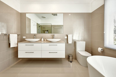 Photo of a bathroom in Melbourne with white cabinets, a freestanding tub, a one-piece toilet, ceramic tile, beige walls and ceramic floors.