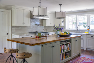 Design ideas for a large country l-shaped eat-in kitchen in Boston with a farmhouse sink, recessed-panel cabinets, white cabinets, wood benchtops, white splashback, ceramic splashback, stainless steel appliances, medium hardwood floors and with island.