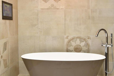 Modern inredning av ett mellanstort grå grått badrum, med möbel-liknande, beige skåp, ett fristående badkar, en toalettstol med separat cisternkåpa, beige kakel, stenkakel, beige väggar, klinkergolv i porslin, ett väggmonterat handfat, bänkskiva i akrylsten och beiget golv