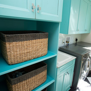 Modelo de cuarto de lavado de galera, exótico, de tamaño medio, con fregadero encastrado, armarios con paneles lisos, puertas de armario azules, encimera de cuarzo compacto, paredes blancas, suelo vinílico, lavadora y secadora juntas y suelo negro