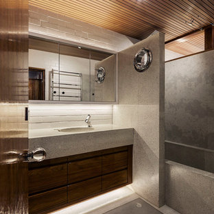 Immagine di una stanza da bagno padronale minimalista di medie dimensioni con ante con riquadro incassato, ante in legno bruno, vasca da incasso, vasca/doccia, WC monopezzo, piastrelle grigie, lastra di pietra, pareti bianche, pavimento alla veneziana, lavabo integrato, top alla veneziana, pavimento grigio e doccia aperta