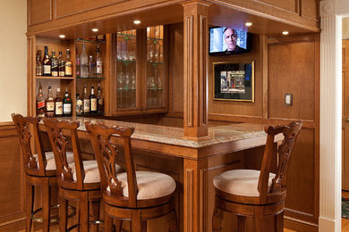 Mid-sized traditional l-shaped wet bar in New York with glass-front cabinets, medium wood cabinets, granite benchtops, medium hardwood floors and brown splashback.
