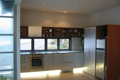 Small beach style l-shaped eat-in kitchen in Wellington with a single-bowl sink, flat-panel cabinets, stainless steel cabinets, glass benchtops, stainless steel appliances, concrete floors and no island.