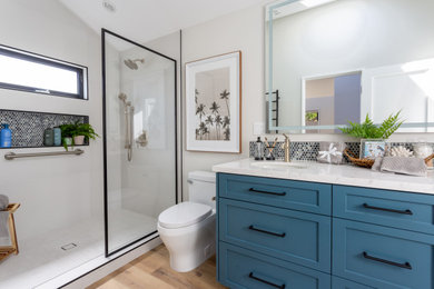 Example of a mid-sized beach style master white tile and porcelain tile vinyl floor, brown floor, double-sink and vaulted ceiling bathroom design in Santa Barbara with shaker cabinets, blue cabinets, a one-piece toilet, white walls, an undermount sink, quartz countertops, white countertops, a niche and a built-in vanity