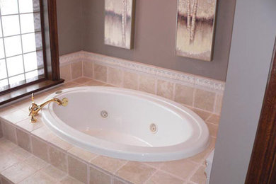 This is an example of a mid-sized traditional bathroom in Indianapolis with a drop-in tub, beige tile and grey walls.