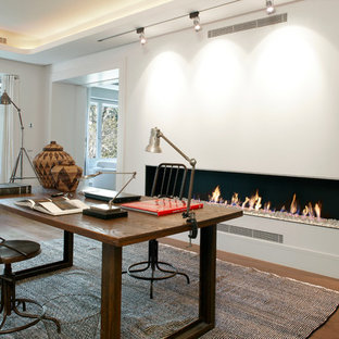 Industriell inredning av ett mellanstort hemmabibliotek, med vita väggar, mörkt trägolv, en bred öppen spis, en spiselkrans i gips och ett fristående skrivbord