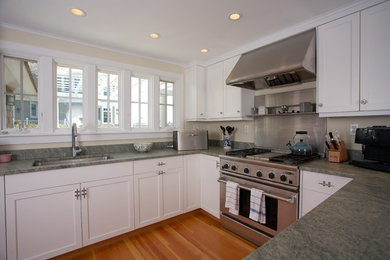 Inspiration for a coastal u-shaped medium tone wood floor eat-in kitchen remodel in New York with an undermount sink, shaker cabinets, white cabinets, granite countertops, stainless steel appliances and a peninsula