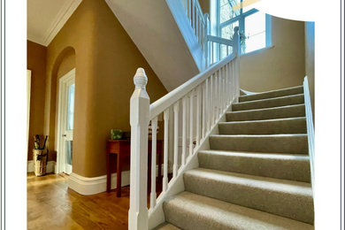 This is an example of a large classic carpeted u-shaped wood railing staircase spindle in Cornwall with carpeted risers.