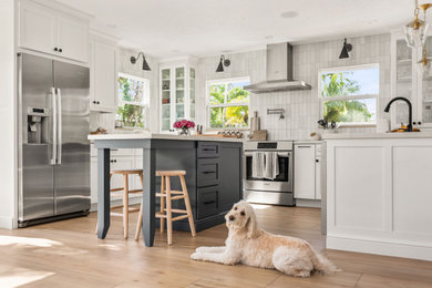 Inspiration for a mid-sized coastal u-shaped medium tone wood floor and brown floor eat-in kitchen remodel in Tampa with an undermount sink, shaker cabinets, white cabinets, quartz countertops, white backsplash, porcelain backsplash, stainless steel appliances, an island and white countertops