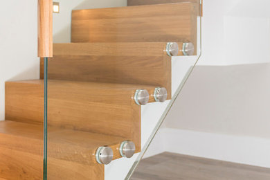 Imagen de escalera suspendida contemporánea de tamaño medio con escalones de madera, contrahuellas de madera y barandilla de vidrio