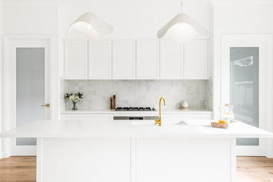 Photo of a contemporary galley kitchen in Sydney with white cabinets, engineered stone countertops, stone tiled splashback, stainless steel appliances, an island and white worktops.