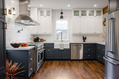 Farmhouse u-shaped brown floor and exposed beam eat-in kitchen photo in Toronto with a farmhouse sink, shaker cabinets, blue cabinets, quartz countertops, white backsplash, subway tile backsplash, stainless steel appliances, a peninsula and gray countertops