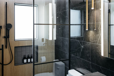 Inspiration for a contemporary 3/4 black tile gray floor and single-sink alcove shower remodel in Houston with flat-panel cabinets, a one-piece toilet, an integrated sink, a hinged shower door, gray countertops, a niche and medium tone wood cabinets