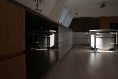 Large contemporary l-shaped open plan kitchen in London with an integrated sink, flat-panel cabinets, grey cabinets, engineered stone countertops, brown splashback, cement tile splashback, stainless steel appliances, light hardwood flooring, an island and white floors.