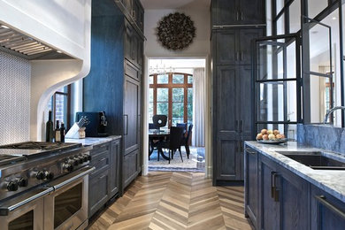 Enclosed kitchen - transitional galley medium tone wood floor and brown floor enclosed kitchen idea in Atlanta with an undermount sink, recessed-panel cabinets, white backsplash, mosaic tile backsplash, stainless steel appliances, no island and blue cabinets
