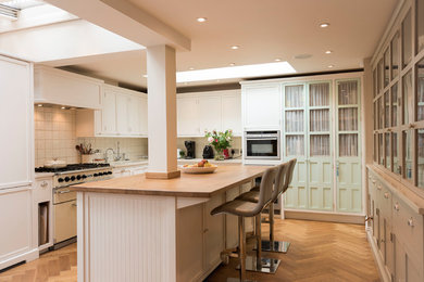 Design ideas for a large traditional u-shaped eat-in kitchen in London with a drop-in sink, shaker cabinets, white cabinets, solid surface benchtops, white splashback, ceramic splashback, coloured appliances, medium hardwood floors, with island, brown floor and beige benchtop.