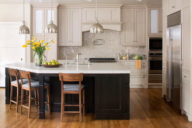 Eat-in kitchen - large traditional l-shaped medium tone wood floor eat-in kitchen idea with quartz countertops, beige backsplash, glass tile backsplash, stainless steel appliances, an island, shaker cabinets and white cabinets
