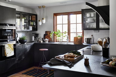This is an example of a large scandinavian u-shaped open plan kitchen in Other with flat-panel cabinets, black cabinets, white splashback, ceramic splashback, brown floor, an undermount sink, black appliances, medium hardwood floors, no island and black benchtop.