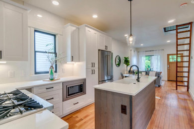 Inspiration for a mid-sized craftsman medium tone wood floor and multicolored floor open concept kitchen remodel in Portland with a farmhouse sink, shaker cabinets, white cabinets, white backsplash, ceramic backsplash, stainless steel appliances, an island and white countertops