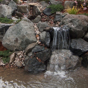 large boulders surround this water fall from above & flows down into larger pond