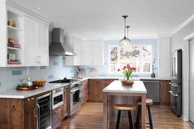 This is an example of a mid-sized transitional u-shaped open plan kitchen with a farmhouse sink, recessed-panel cabinets, quartz benchtops, blue splashback, stainless steel appliances, medium hardwood floors, with island, yellow floor, white benchtop, medium wood cabinets and window splashback.