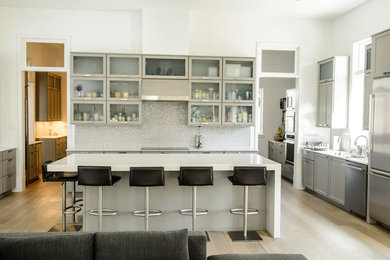 Inspiration for a mid-sized modern l-shaped light wood floor eat-in kitchen remodel in New Orleans with a drop-in sink, glass-front cabinets, gray cabinets, quartzite countertops, stainless steel appliances and an island