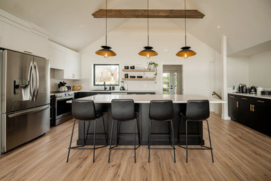 Large modern u-shaped open plan kitchen in Other with flat-panel cabinets, black cabinets, white splashback, stainless steel appliances, an island, brown floors, white worktops and a vaulted ceiling.