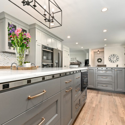 Example of a huge farmhouse l-shaped medium tone wood floor and brown floor eat-in kitchen design in Milwaukee with a farmhouse sink, shaker cabinets, gray cabinets, quartz countertops, white backsplash, marble backsplash, stainless steel appliances, an island and gray countertops